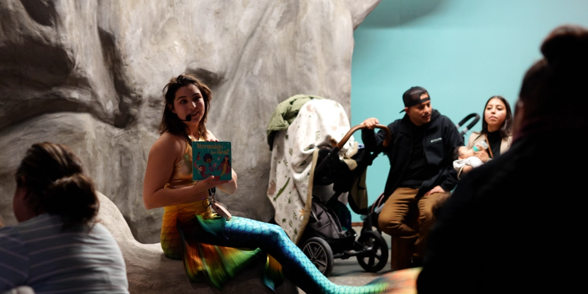 A woman dressed up as a mermaid reading to a group